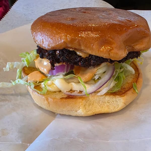 Close-up of a Khorasan Kabab burger with lettuce, red onion, and sauces on a bun.