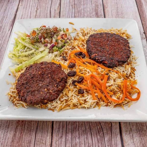 Two Afghan kabob patties with rice, shredded carrots, raisins, and a side salad on a white plate.