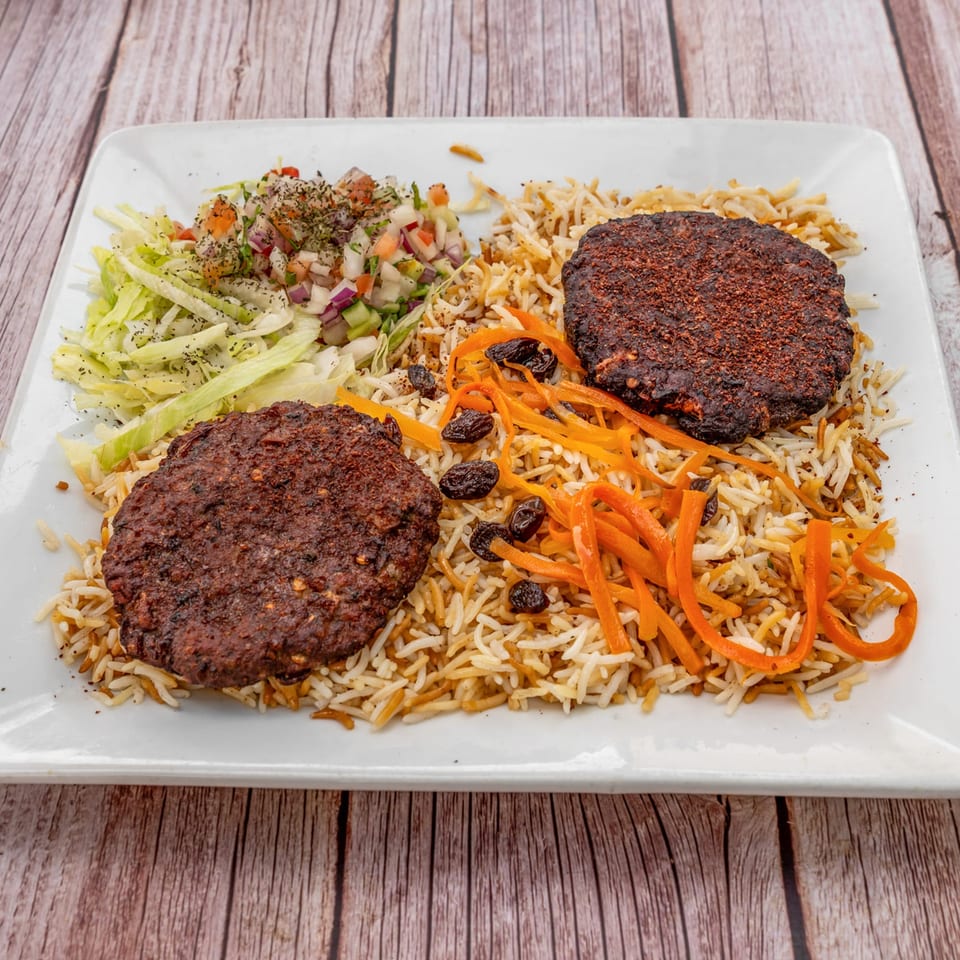 Two Afghan kabob patties with rice, shredded carrots, raisins, and a side salad on a white plate.