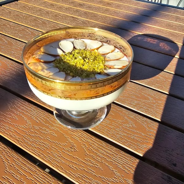 Afghan dessert in a gold-rimmed glass, topped with sliced almonds and green pistachio crumbles.