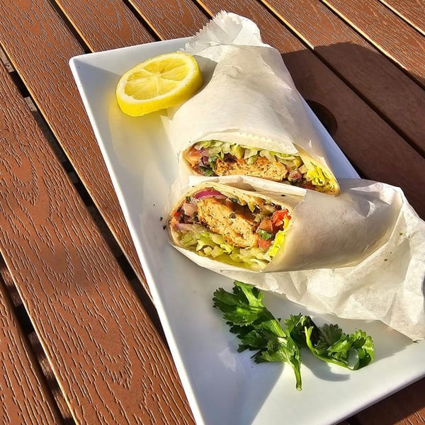 Two halves of a chicken wrap with lettuce, tomatoes, and onions, served with a lemon wedge and parsley.