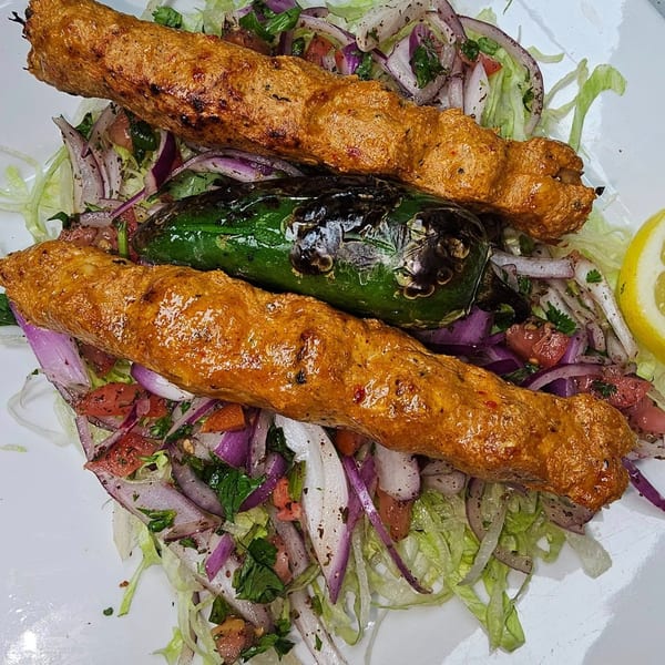 Two grilled Khorasan Kabab skewers with a charred green pepper, served over a fresh salad.