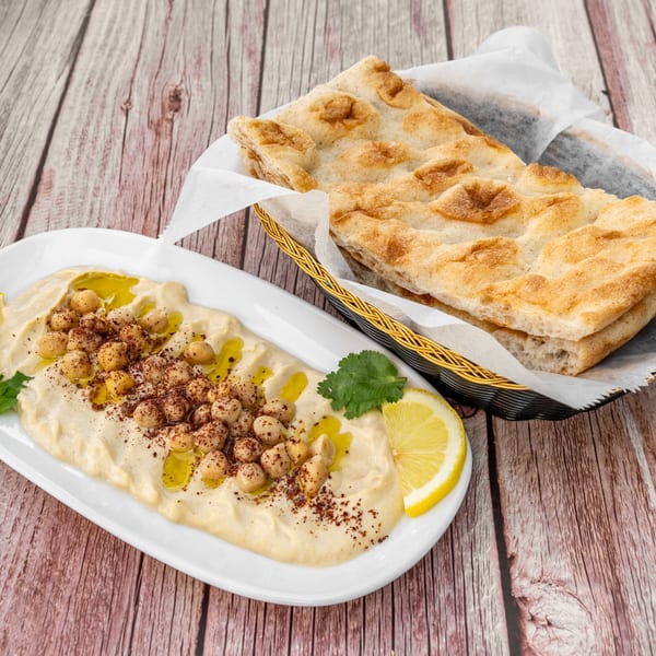 Hummus topped with chickpeas, olive oil, and spices, served with flatbread in a basket.